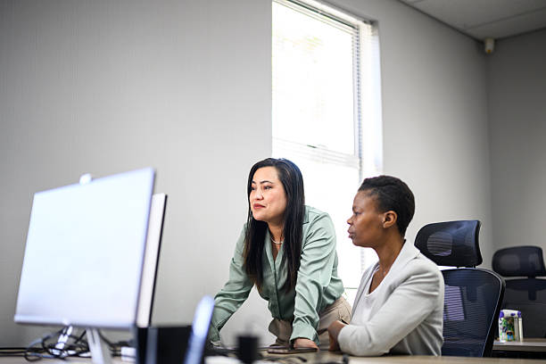 istock Side view of two professional women collaborating on a computer at a desk in a modern corporate office 2243805036