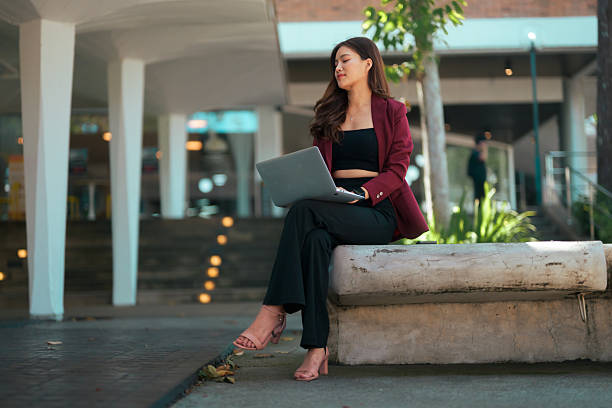 istock Professional young businesswoman using her laptop for remote work while sitting outdoors on a city bench, looking away 2243805426
