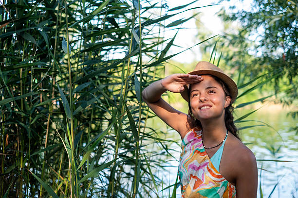 Young woman in a straw hat shielding eyes from sun, looking away happily by the lake