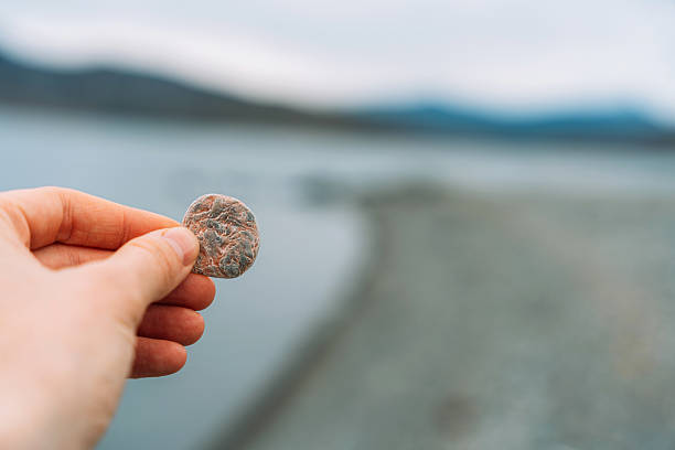 Hand holding small smooth pebble by lakeshore. High quality photo