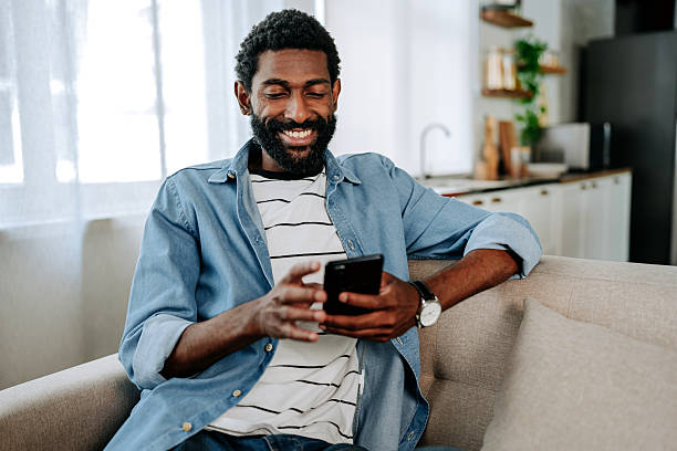 istock Smiling man sitting on sofa using smartphone at home 2243821167