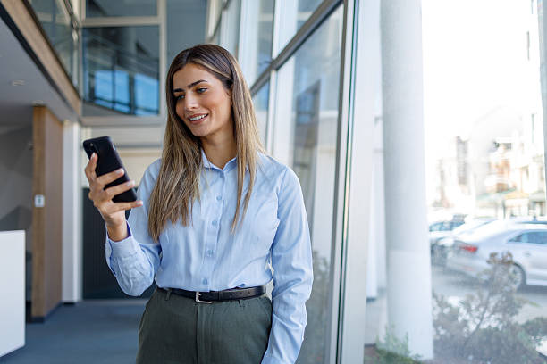 istock Businesswoman focused on her smartphone in a bright office building, smiling while texting or browsing, connecting people 2243824557