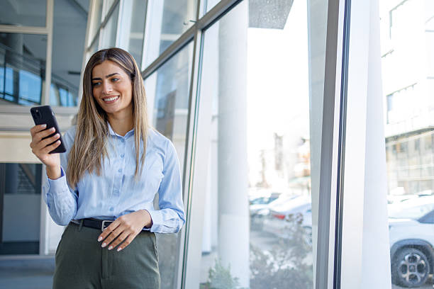 istock Businesswoman standing near large window, sending message, checking email, or browsing app on her mobile phone 2243824706