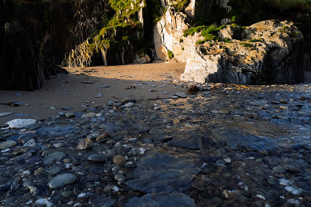 Water rushes over rocks at low tide as it flows toward a sandy cove surrounded by rocky cliffs. The scene is captured in West Cork, Ireland.