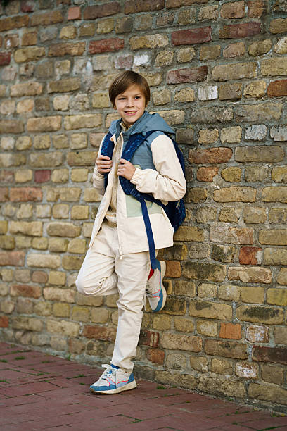 istock Schoolboy wearing backpack leaning against brick wall smiling 2243826819
