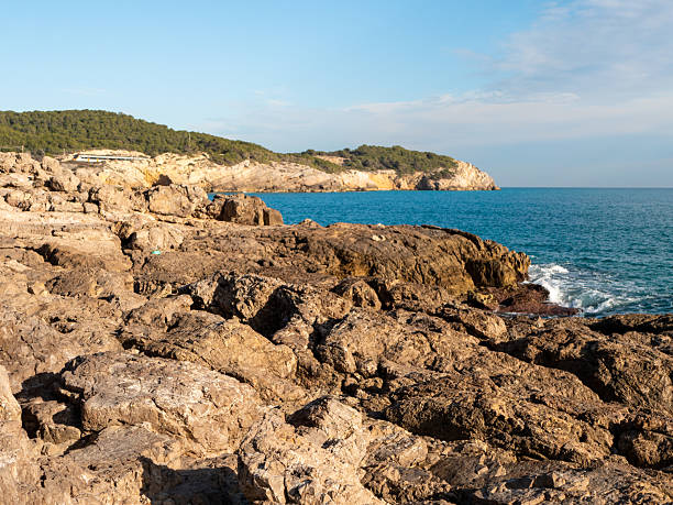 istock Bright sunlight shines on rugged rocks along coastline with vibrant blue waters. lush green hills in background add serenity to natural coastal scene at midday 2243827108