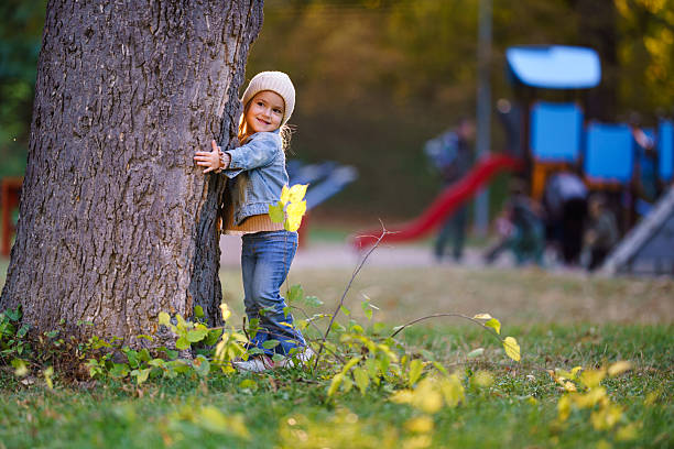 Young girl smiling and hugging a tree playing outside on a sunny autumn day.