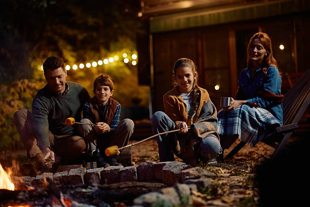 istock Happy family gathering around campfire and roasting corn in the evening. 2243828700