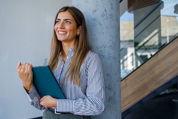 istock Professional businesswoman in modern office smiling while holding digital tablet, contemplating future business 2243830631