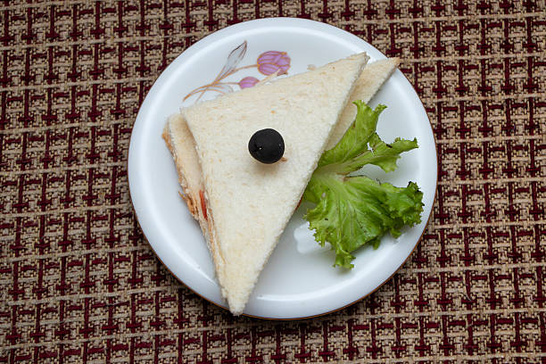 Chicken Sandwich crisp white bread sandwiches with fresh lettuce and a black olive skewer served on a decorative plate