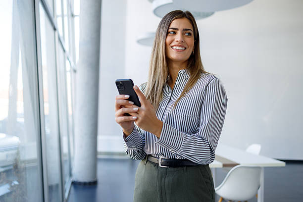 istock Young businesswoman smiling while checking messages or browsing on a smartphone in a bright office environment 2243832256