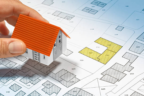 istock HAND PLACING A MODEL HOUSE ON A FICTIONAL CADASTRAL MAP - Architectural planning and real estate development cpncept 2243834680