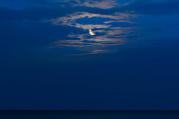 Crescent moon reflecting over calm ocean at night