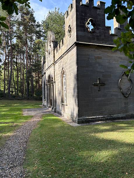 istock A charming stone building with gothic windows and battlements stands amid lush greenery. Pointed arches and ornate details give it a castle-like elegance, blending history with serene natural beauty. 2243841727