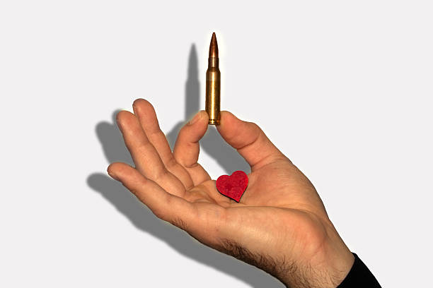 A hand holds a bullet vertically while supporting a small red heart, highlighting the stark contrast between violence and love. A powerful message about choice and humanity.