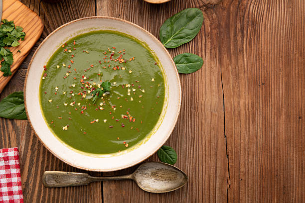 Bowl of homemade green spinach cream soup topped with cheese and fresh parsley, served on wooden rustic background with spices.