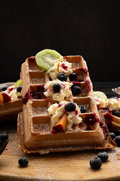 Crispy waffles topped with whipped cream, blueberries and kiwi slices, decorated with sugar on rustic background.