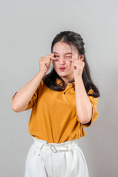 istock Young Asian woman makes a cute crying face while pointing to her eyes with both index fingers. Her playful and dramatic expression conveys mock sadness or teasing emotion. 2243851548