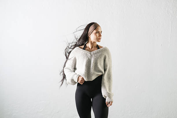 A confident and athletic woman wearing modern fitness clothing standing against a white background, representing strength, wellness, motivation, and a healthy active lifestyle.