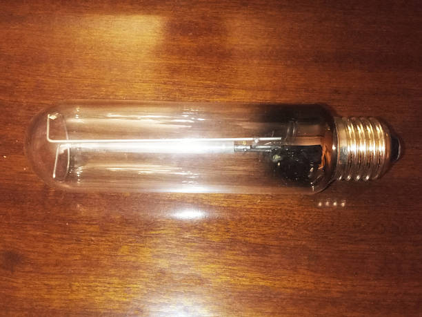 A clear, cylindrical high-pressure sodium (HPS) lamp bulb rests horizontally on a dark wooden table