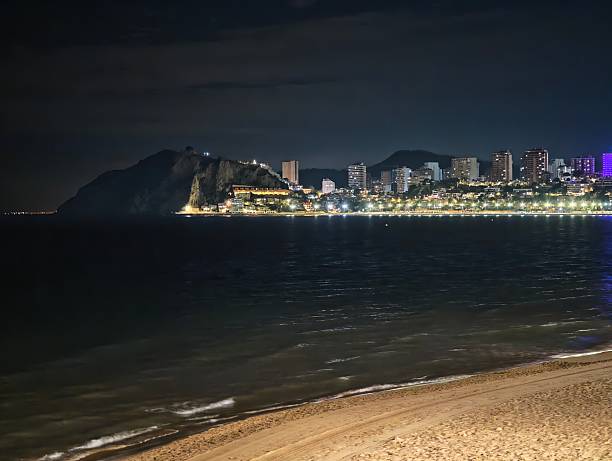 istock sandy coast at night, peaceful shoreline with distant bright cityscape reflecting on dark sea 2243855518