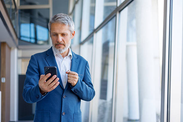 istock Mature executive standing and looking at cell phone, engaging in online communication or business networking 2243857443