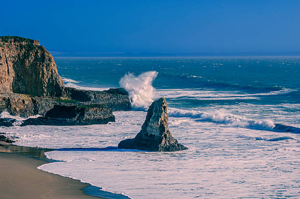 Ocean waves crashing on rocky cliffs and sandy beach, off California coast.Taken on Davenport Beach, California, USA.