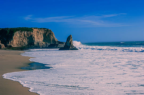Ocean waves crashing on rocky cliffs and sandy beach, off California coast.Taken on Davenport Beach, California, USA.