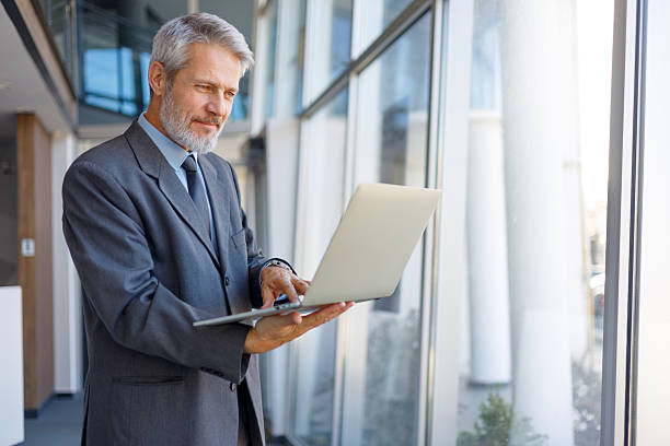 istock Mature businessman standing, looking at laptop in modern office, working with remote technology connection 2243858367