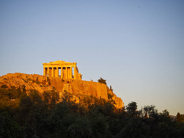 Ancient Parthenon temple on Acropolis hill illuminated by warm golden sunset light in Athens