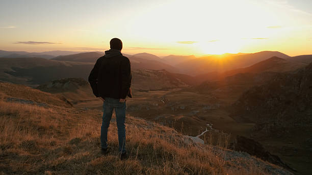 istock Man standing on a mountain ridge watching the sunset over the valley on a clear evening 2243864931