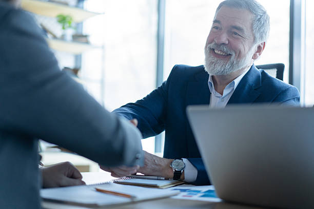 istock Happy businessmen shaking hands at group board meeting 2243865277