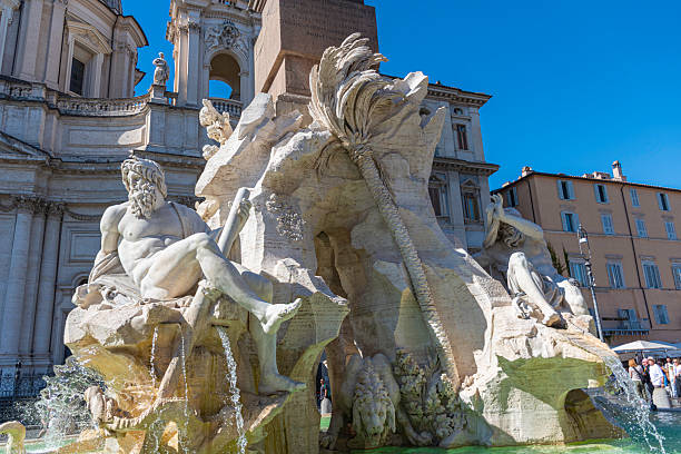 Rome, Italy - October 13, 2025: Detail of the Fountain of the Four Rivers (Fontana dei Quattro Fiumi) in Piazza Navona, Rome, Italy. The Baroque masterpiece by Gian Lorenzo Bernini features a marble statue representing the river gods, flowing water, and an ancient Egyptian obelisk in the background. The Church of Sant’Agnese in Agone and its domes can be seen behind the fountain on a bright sunny day.
