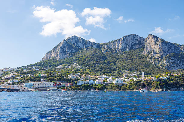 Capri, Italy - 04.29.2025: View from the sea to the cliffs of the coast of the island of Capri with partial tree cover in spring colors. Beautiful views.