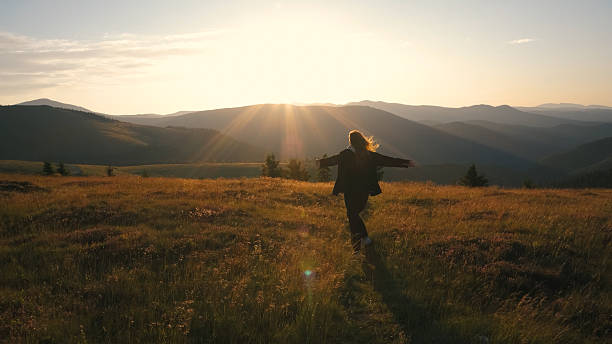 Woman enjoying a sunset in a mountain meadow while spinning joyfully with arms outstretched