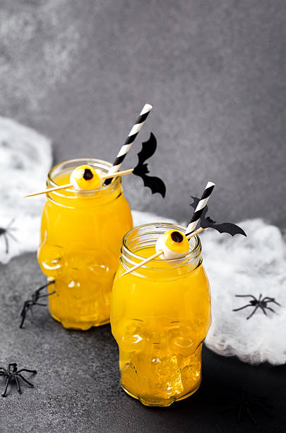istock Two yellow drinks in skull glasses decorated with candy eyeballs and bat picks surrounded by fake spiders and cobwebs 2243874954