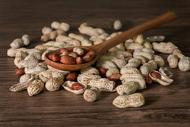 Shelled and Unshelled Peanuts and Wooden Spoon on a Rustic Dark Brown Wood Table stock photo