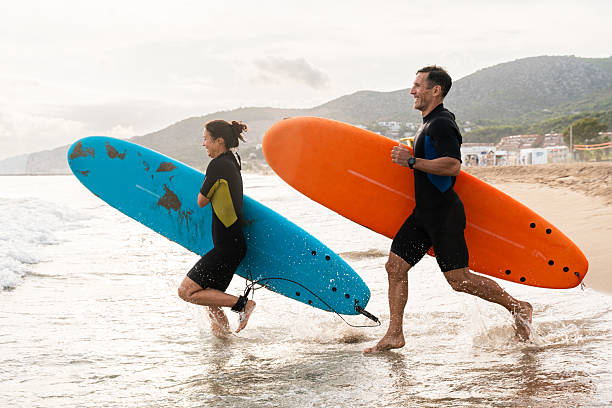 istock Couple running into ocean with surfboards at sunset 2243911071