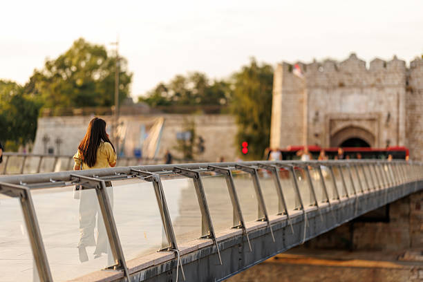 Asian woman talking on smart phone while crossing city bridge on the way from work, with medieval fortress in background in city of Nis Serbia
