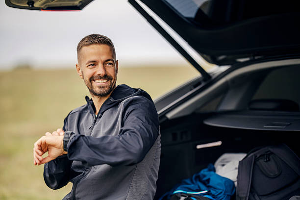 istock Man smiling checking smartwatch next to open car trunk 2243920034