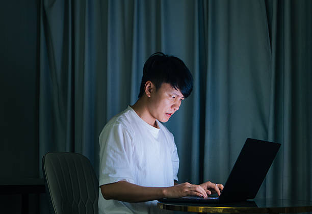 istock Young Asian man working at home on laptop at night, focused on remote work and digital lifestyle, representing modern technology, productivity, and contemporary home office culture in urban living. 2243920949