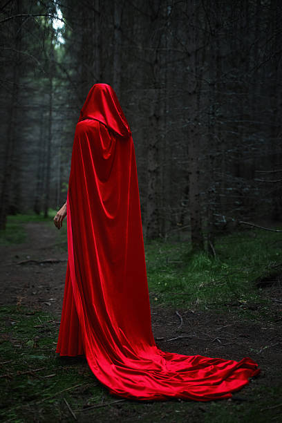 istock figure draped in a flowing red cloak strolls along a narrow path in a dense, shadowy forest. morning light barely penetrates the thick trees, creating an eerie atmosphere 2243922613