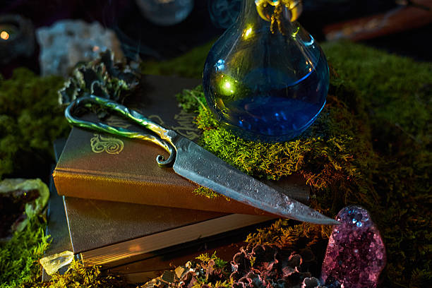 istock dark, enchanting scene features a silver dagger resting on an ancient book. blue potion glimmers nearby, surrounded by moss and mystic crystals, creating a magical atmosphere 2243925766