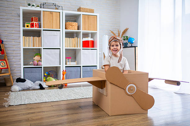 istock Cute boy dressed as a pilot pretends to fly in a cardboard box airplane, showing creativity and childhood imagination. 2243930925