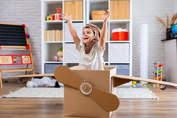 istock Cute boy dressed as a pilot pretends to fly in a cardboard box airplane, showing creativity and childhood imagination. 2243931653