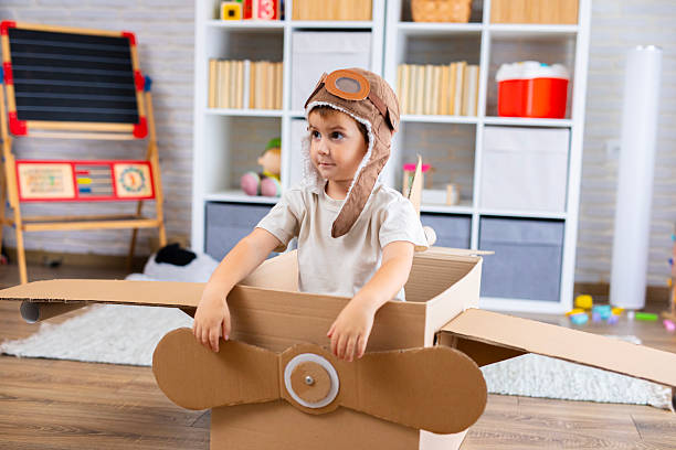 istock Cute boy dressed as a pilot pretends to fly in a cardboard box airplane, showing creativity and childhood imagination. 2243931672