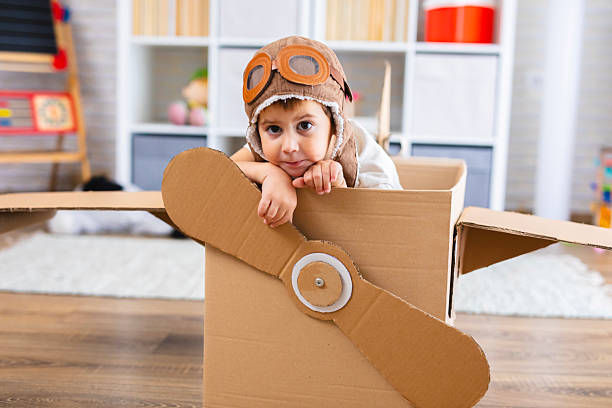 istock Cute boy dressed as a pilot pretends to fly in a cardboard box airplane, showing creativity and childhood imagination. 2243932257