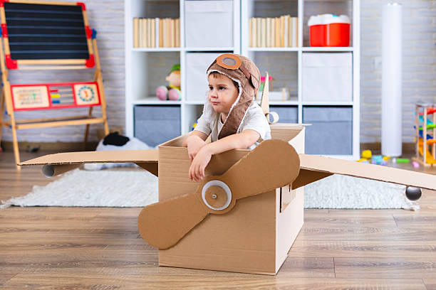 istock Cute boy dressed as a pilot pretends to fly in a cardboard box airplane, showing creativity and childhood imagination. 2243932292