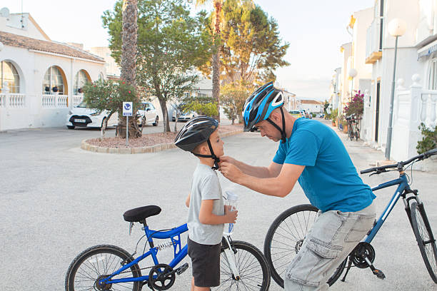 A father fastens his son's protective helmet before a bicycle ride.