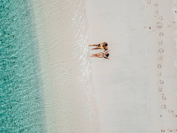 Man and woman in swimwear lying on pristine white sand near clear turquoise water. Happy couple enjoying beach vacation and summer fun. Romantic seaside holiday moment.